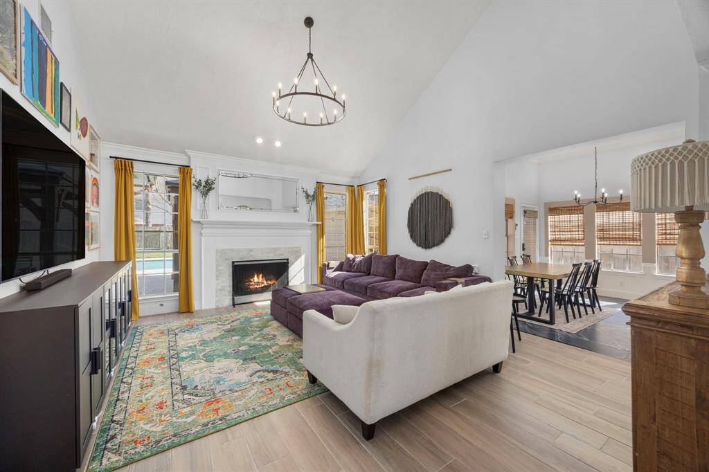 Stunning living room with tile surround fireplace flanked with windows overlooking the backyard, soaring ceilings, and a chandelier.