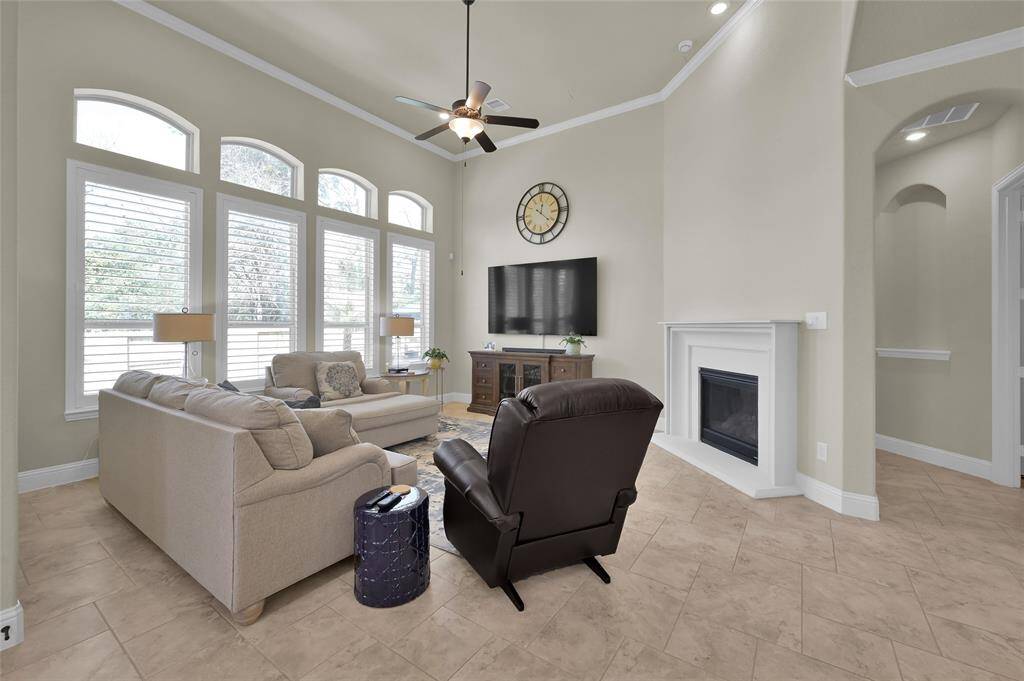 Bask in the serene glow of this inviting living room featuring soft natural light, custom shutters, ceiling fan, easy to maintain tile flooring, crown molding and a cozy warm gas-log fireplace for those chilly evenings.