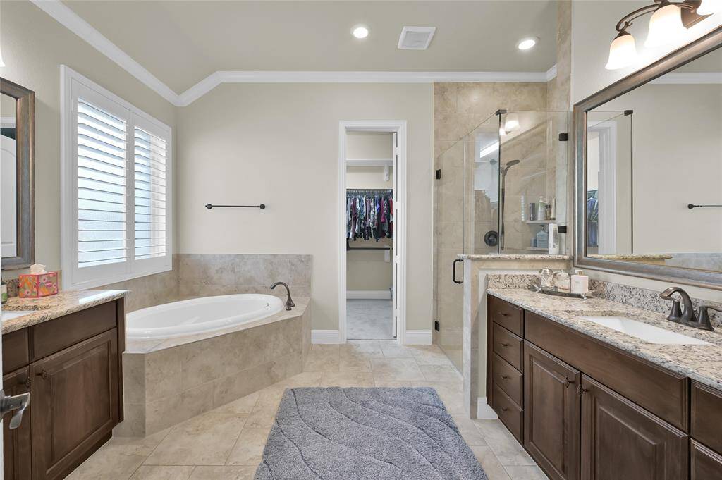Primary bathroom offers dual vanities with plenty of storage, rich wood cabinets, large framed mirror and an abundance of natural light.