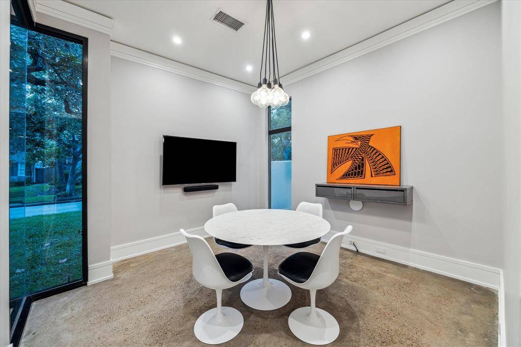 The study/home office is away from the living area and overlooks the front door walkway and sidewalk.  Note the inoperable plate glass windows, offering floor to ceiling views and security.  TV, soundbar and mounted floating storage cabinet remain.  Note the chandelier, complementary to the dining room fixture.