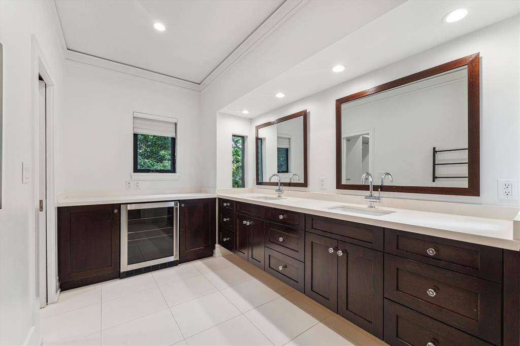 The Primary bathroom offers dual vanity sinks and a coffee bar with drink refrigerator below.  The timeless design of neutral countertops and tile accentuate the elegant cabinetry.  The first of two closets is accessed through the door on the left.