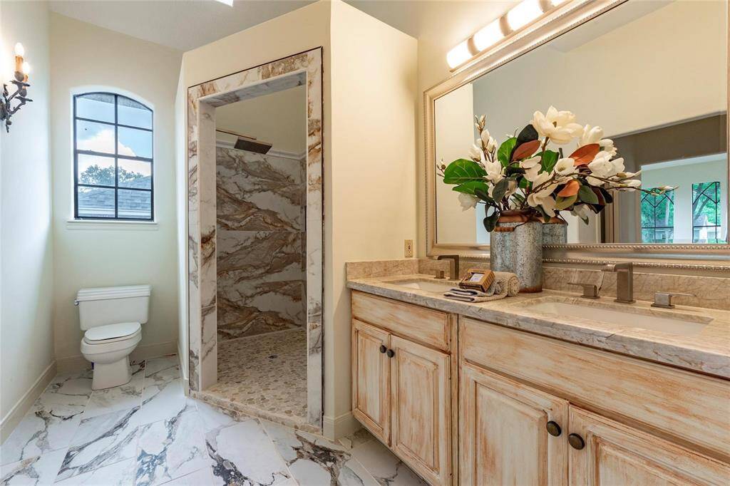 Beautifully updated primary bathroom with mounted sconce lighting, framed mirror, recently installed tile flooring, his/her sinks and tiled walk-in shower.