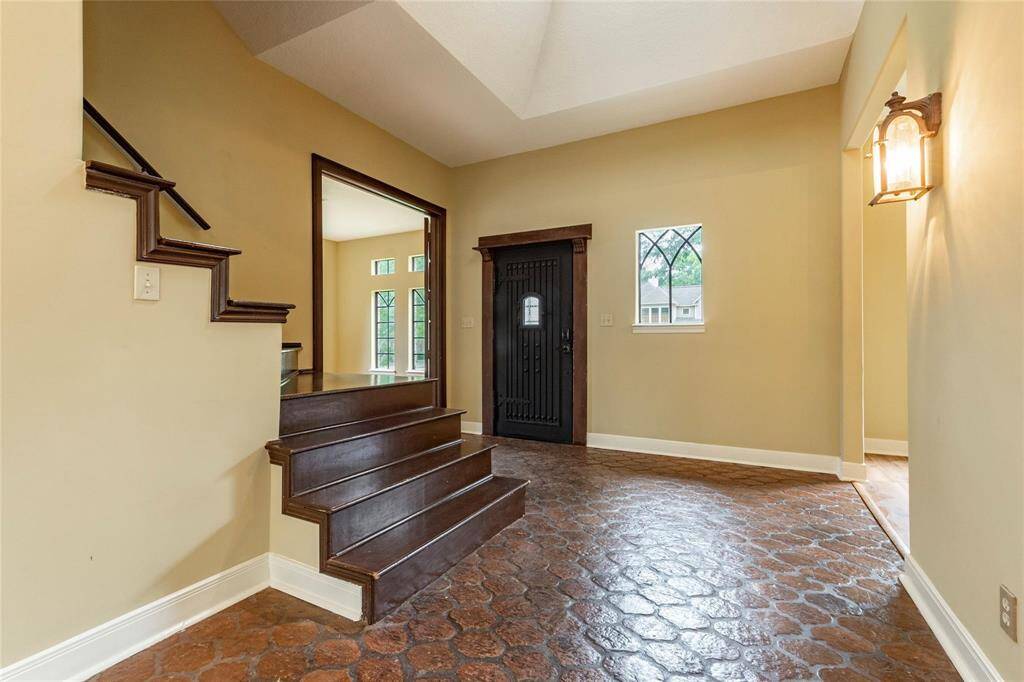 Tiled entryway with high ceilings heavy door and staircase leading to 2nd level.