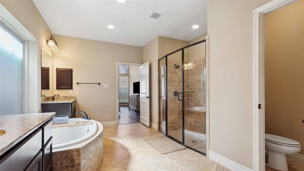 The primary bath boasts his-and-her vanities, ample storage, and two large separate closets with dark-colored cabinets, creating an inviting primary bath retreat.