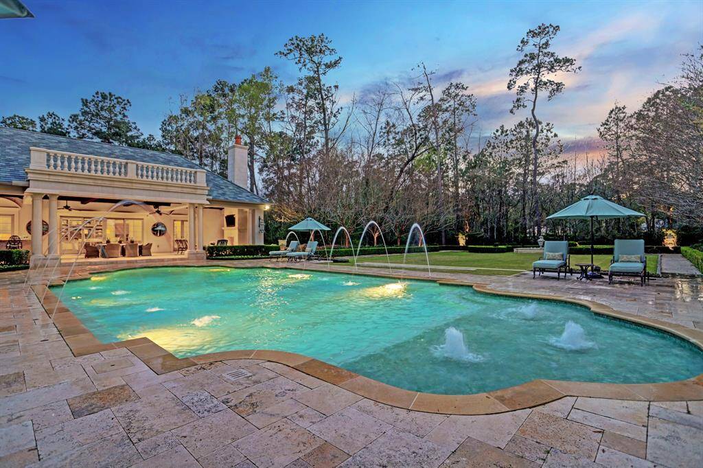 Take a plunge into the 10-foot deep end of the pool, surrounded by lush greenery and vibrant blooming gardens, offering a serene escape from the summer heat, with the pool house gracefully overlooking the scene.