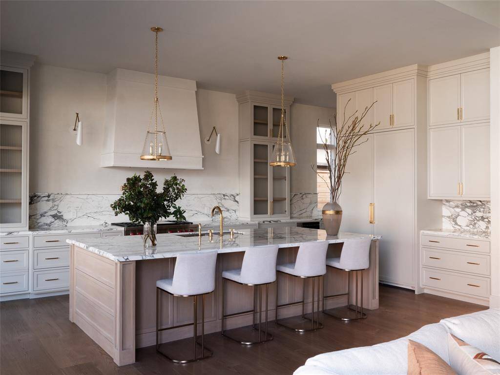 This stunning chef’s kitchen is designed for both function and style, featuring a sprawling marble island that serves as the centerpiece. The marble backsplash extends seamlessly behind the Wolf dual fuel range, complemented by a striking custom plaster vent hood. Flanking the range are Aerin double wall lights and custom-built glass-front cabinetry, offering both display and storage space.