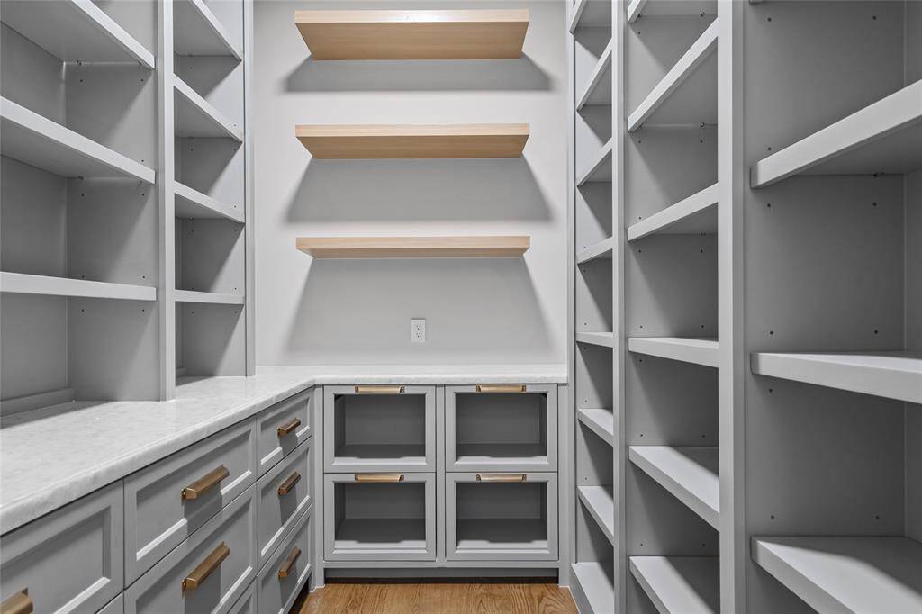 Offering exceptional storage and organization, the walk-in pantry is thoughtfully designed with marble counters for a refined yet functional workspace. Custom-built cabinetry pairs beautifully with floating white oak shelves, while metal mesh front drawer storage adds a stylish touch. The warm white oak hardwood floors complete the space, creating a seamless blend of elegance and practicality.