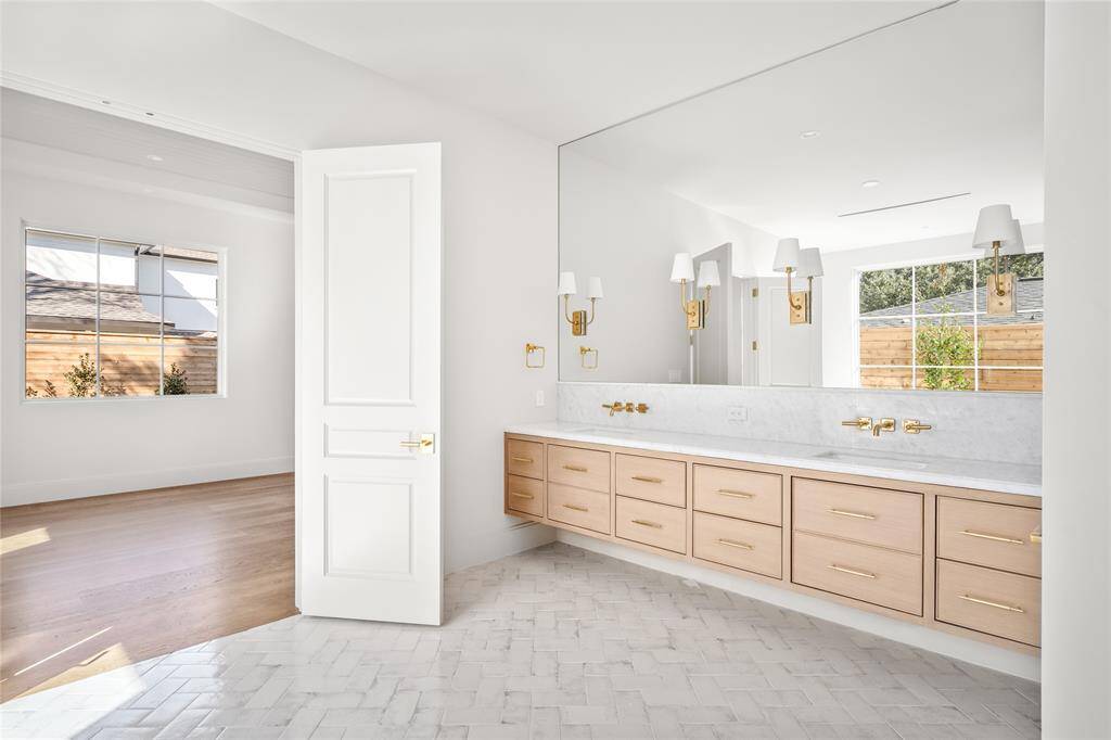 the ensuite bathroom for this dual purpose room features a beautiful marble dual vanity complemented by refined brass pulls. Thomas O’Brien sconces add a touch of designer sophistication, while a textured subway tile floor enhances the space with subtle depth. A private water closet offers added convenience, and direct access to a spacious walk-in closet ensures seamless organization.