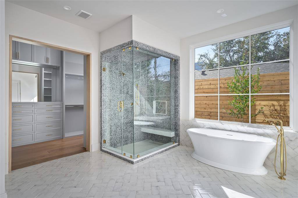 Designed for ultimate relaxation, the ensuite bathroom boasts a frameless, glass-enclosed shower with a built-in bench, offering a sleek and modern aesthetic. Adjacent to it, the pedestal soaking tub serves as a luxurious focal point, perfect for unwinding. Both feature elegant brass plumbing fixtures, enhancing the space with timeless sophistication.