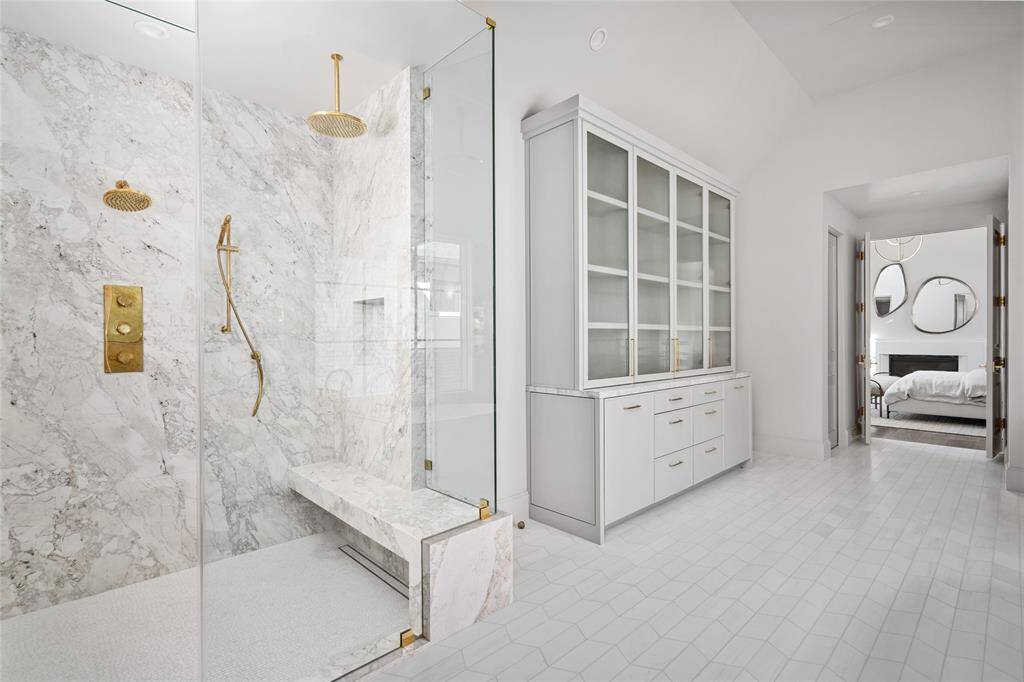 Elevating everyday luxury, the primary ensuite bath features an oversized walk-in shower with stunning glass entry, luxurious marble walls, and is outfitted with a premium Waterworks shower kit. Custom-built glass-front cabinetry provides ample storage and is anchored by an elongated chevron marble tile floor, completing this luxurious retreat.