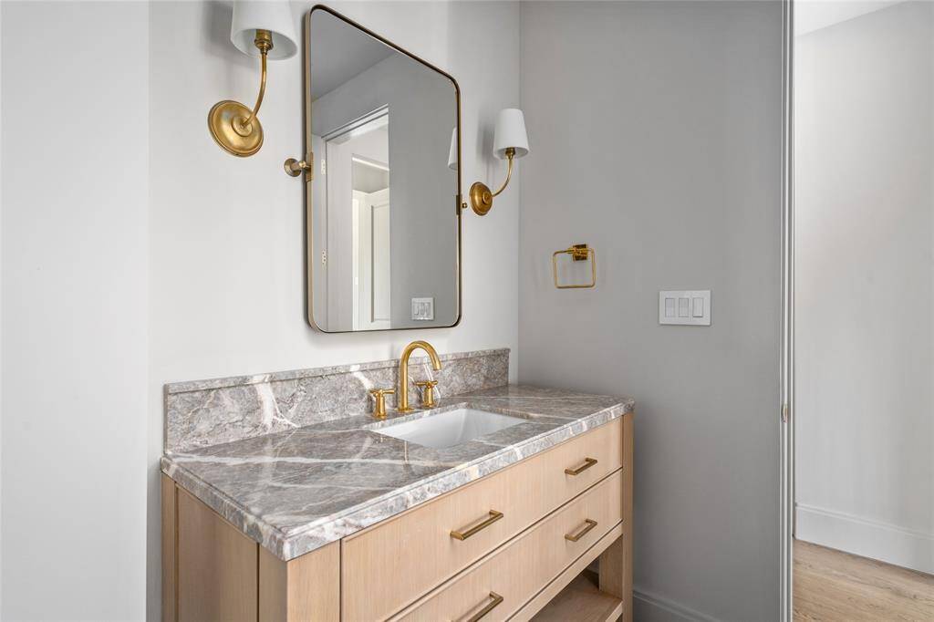 Refined and elegantly appointed, this ensuite bathroom features a stunning marble vanity accented by designer Aerin sconces, which complement the sophisticated herringbone tile floors. Just out of frame, the glass-entry walk-in shower is a true statement piece, showcasing a striking combination of marble and subway tile walls. This luxurious space seamlessly blends modern design with timeless materials.