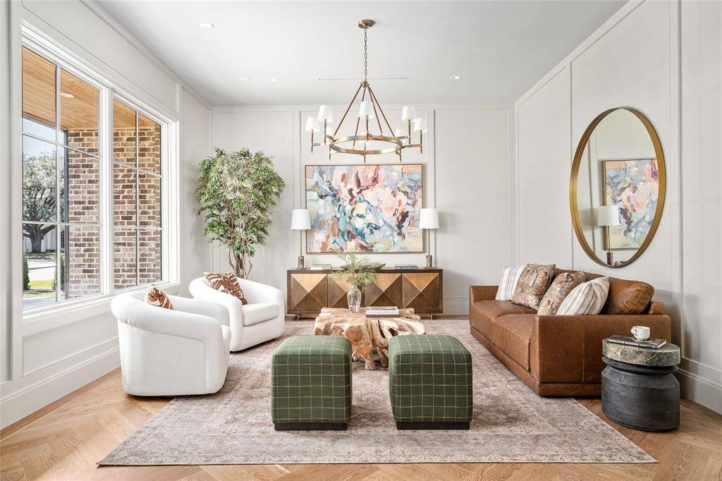 Exuding timeless elegance, this formal living room is anchored by a striking Ralph Lauren chandelier that casts a warm, inviting glow. Refined wall paneling adds depth and sophistication, while a large picture window floods the space with natural light. The herringbone white oak hardwood floors with a brass inlay border complete the room with a touch of luxury.