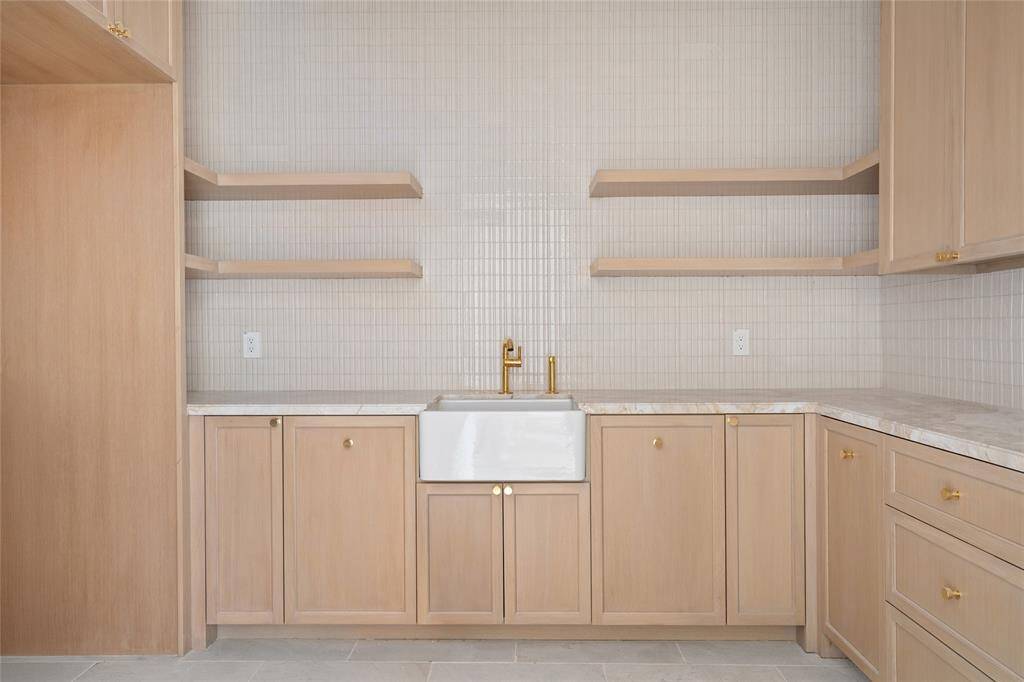 Blending functionality with elegance, the laundry room features marble countertops and a classic farmhouse apron-front sink. Custom-built cabinetry and open shelving provide ample storage, while a skylight fills the space with natural light. The limestone tile floor adds a refined touch, completing this beautifully designed and highly practical workspace.