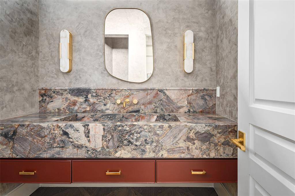 A striking blend of bold design and luxurious materials defines this secondary bathroom. The apron-front marble vanity with an integrated sink serves as a dramatic focal point. Softly textured Venetian plastered walls and ceiling add depth and warmth, while Kelly Wearstler sconces provide a sculptural lighting element. Below, white oak hardwood floors in a custom interlacing pattern complete the space with a refined and sophisticated touch.