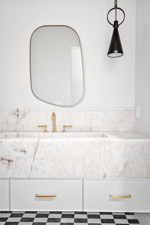An upstairs powder room showcases a magnificent quartzite vanity with an integrated sink and sleek under-mount drawers. Overhead, Suzanne Kasler pendants add a touch of industrial charm, while classic cottage checkered tile floors bring a timeless, vintage-inspired appeal to the space.