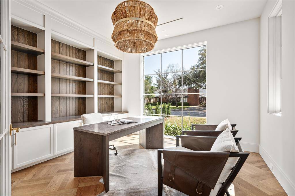 This elegant study features glass French doors, a large picture window with scenic south lawn views, and custom built-ins with beautiful brass pulls. White oak hardwood floors with a custom design add character, while a Drew & Jonathan hanging shade brings warmth.