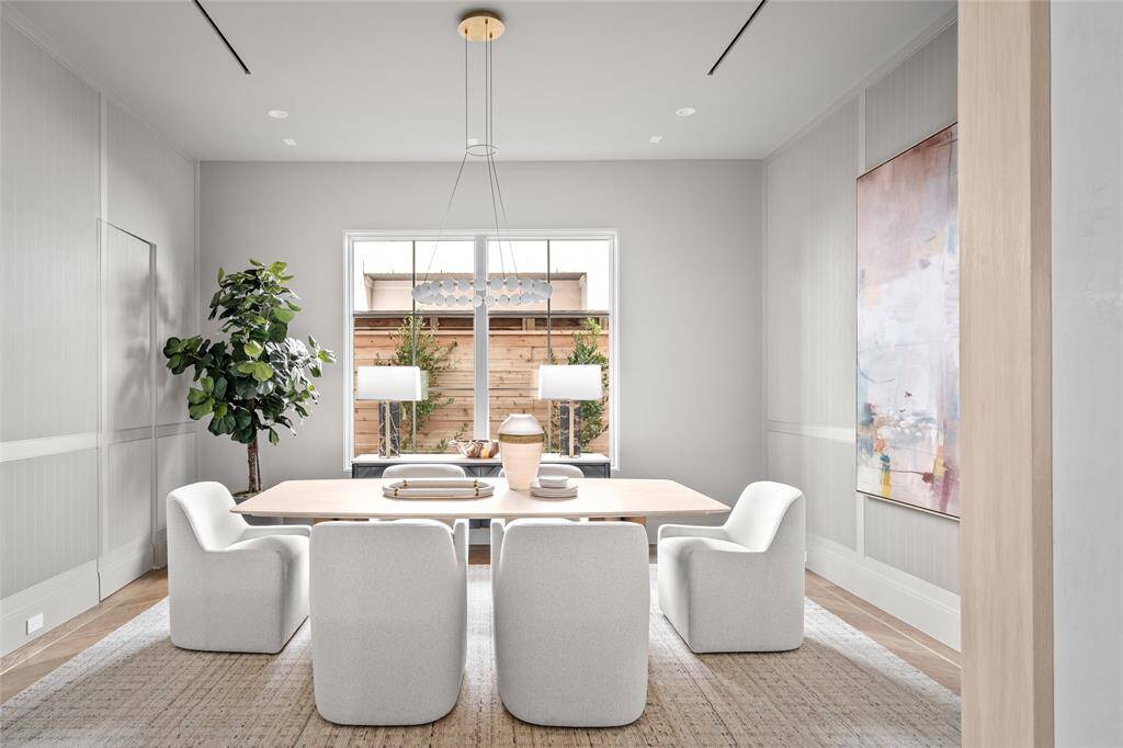 This refined dining room exudes sophistication, anchored by a striking Sean Lavin chandelier that casts a warm, inviting glow. Two fixed glass windows provide natural light and serene views, enhancing the airy ambiance. The space is grounded by stunning herringbone white oak hardwood floors with a brass inlay border, adding a touch of luxury to this thoughtfully designed setting.