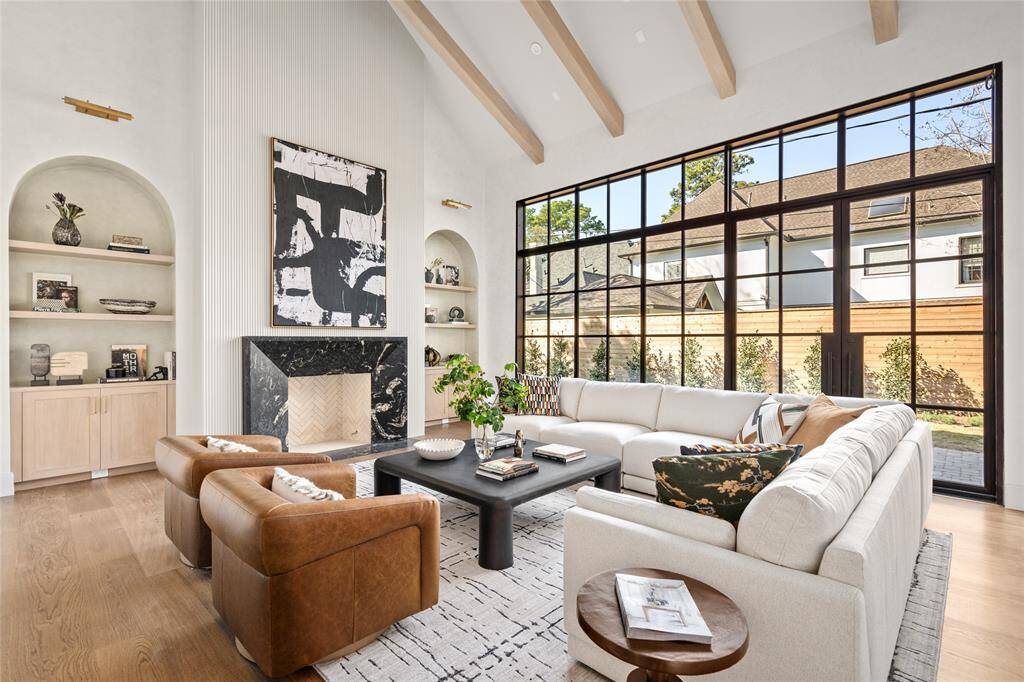 Enter into the breathtaking open-concept family room, featuring a gas fireplace with a custom granite surround on a fluted accent wall. Expansive steel French doors and windows bathe the space in natural light, offering seamless indoor-outdoor living with direct access to the backyard and outdoor kitchen.
