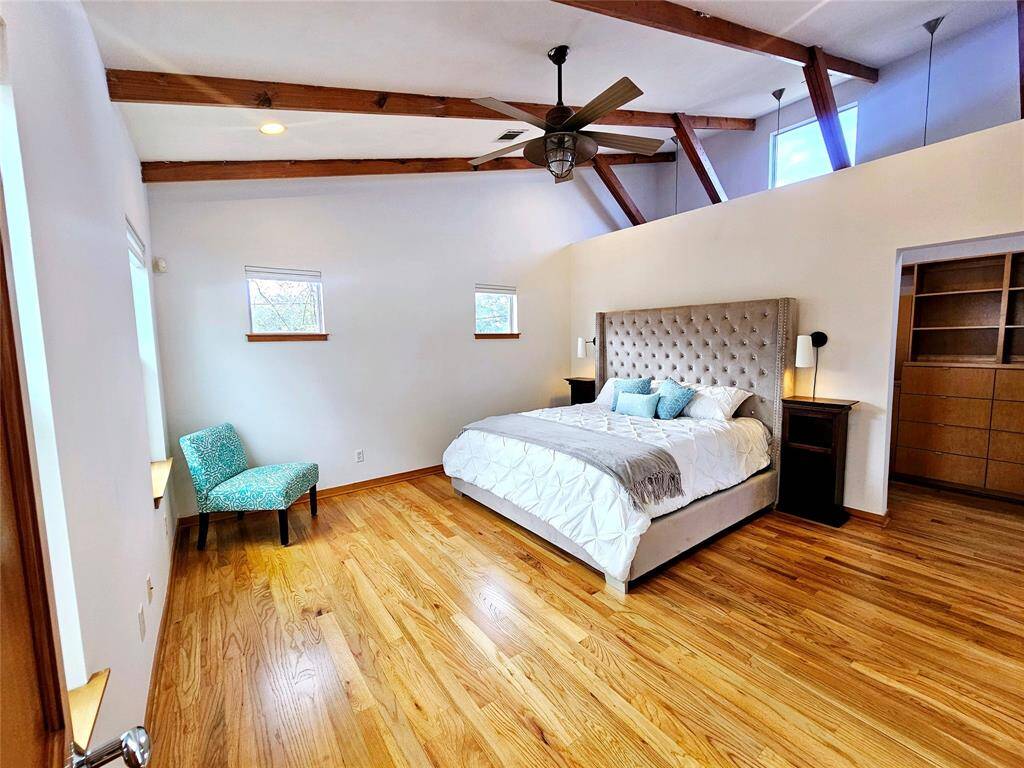 stunning, private primary bedroom with vaulted ceiling and exposed beams along with hardwood floors.