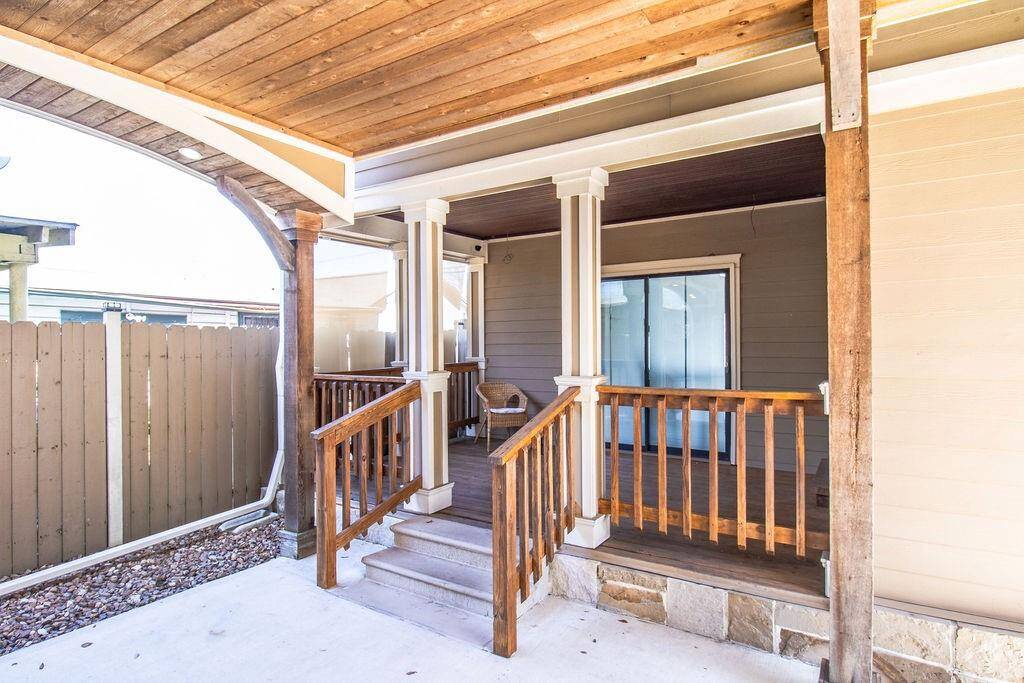 This photo showcases a cozy covered porch with wooden railings and pillars. It features a sliding glass door leading inside, and a privacy fence surrounds the area, creating a welcoming and private outdoor space.