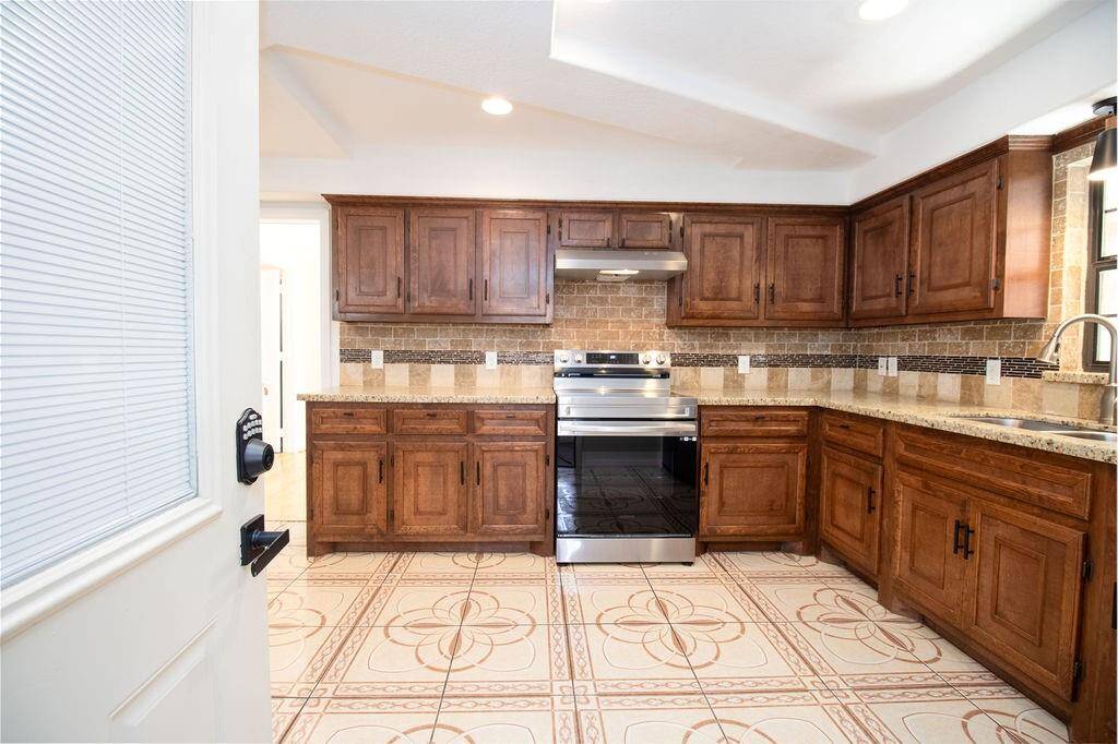Spacious kitchen featuring rich wood cabinetry, stainless steel appliances, and decorative tile flooring. The room is well-lit with natural and overhead lighting, offering ample counter space for cooking.