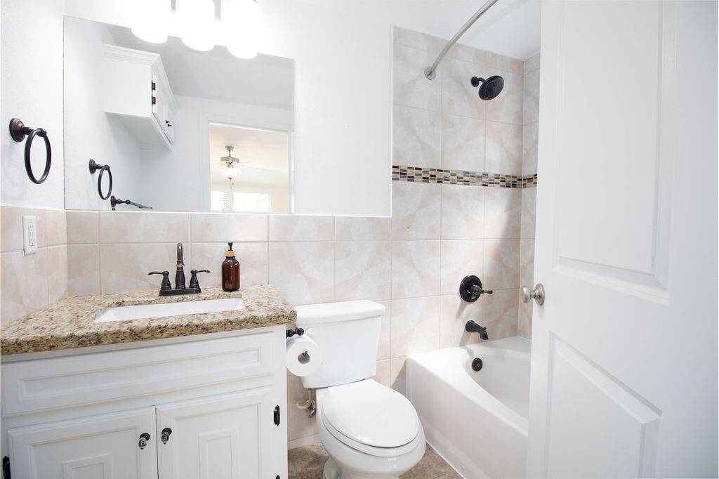 This 2nd full bathroom in the downstairs guest bedroom features a clean and modern design with a granite countertop, white cabinetry, and a tiled shower-tub combo. The neutral tile backsplash with a decorative strip adds a touch of elegance.