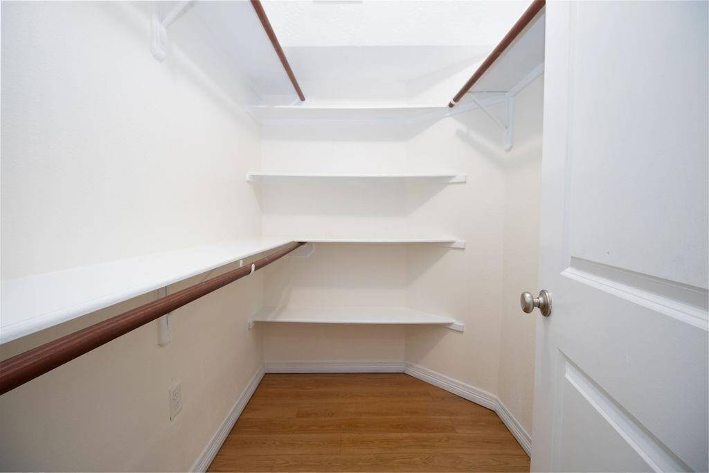 This is a spacious walk-in closet featuring multiple shelves for storage and hanging rods on both sides, complemented by a light wood floor and white walls for a clean, bright look.