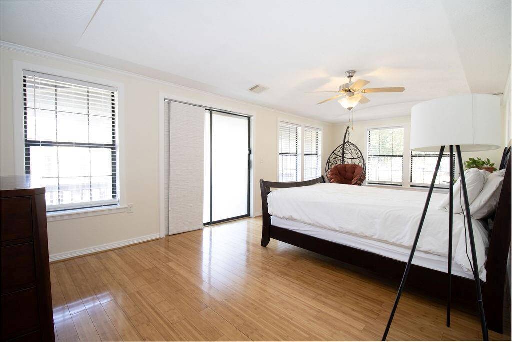This spacious master bedroom features has LVP floors, ample natural light from large windows, and a ceiling fan. It includes sliding doors leading to a private outdoor space.