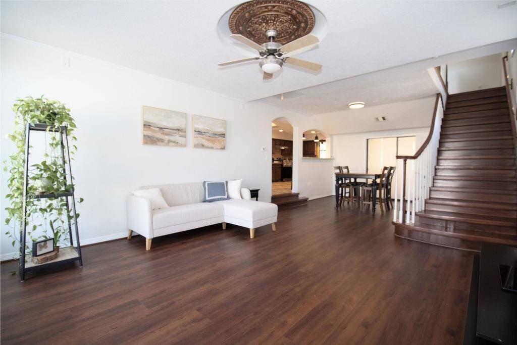 This spacious living area features rich LVP floors, and unique ceiling fan. It seamlessly connects to the dining area and kitchen. The elegant staircase adds charm and leads to the upper level, while large windows provide ample natural light.
