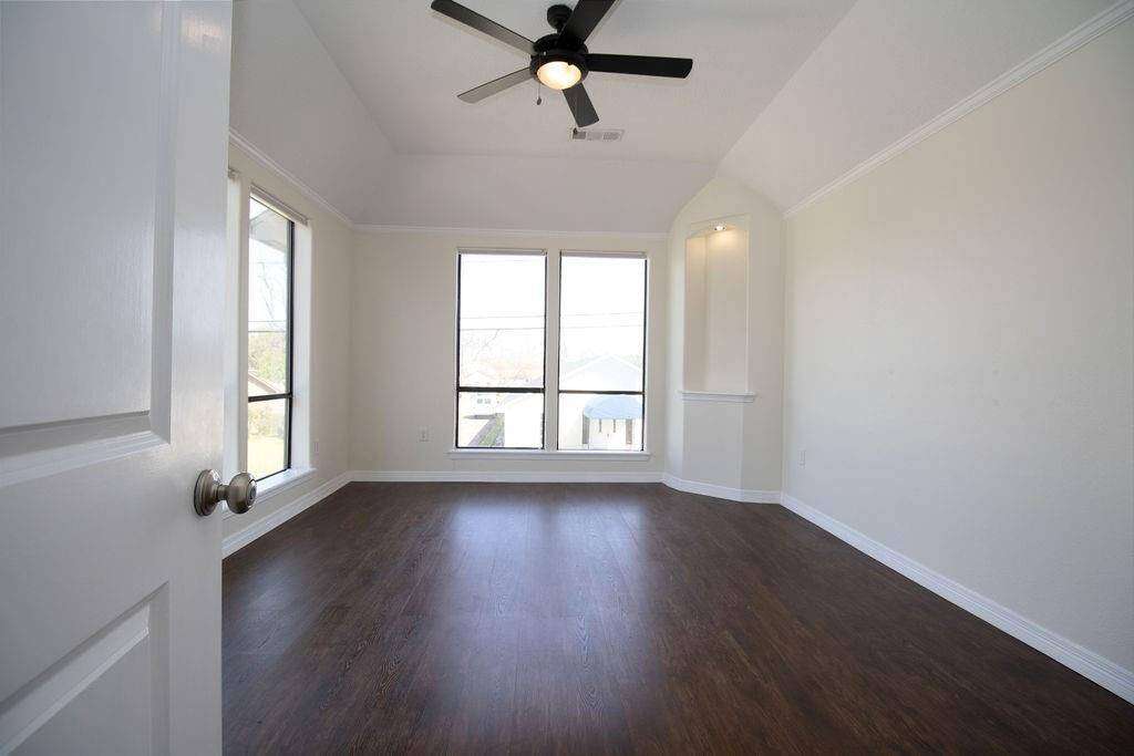 This is second bedroom upstairs features high ceilings with a modern ceiling fan, large windows offering ample natural light, and dark LVP flooring, creating a bright and spacious atmosphere.