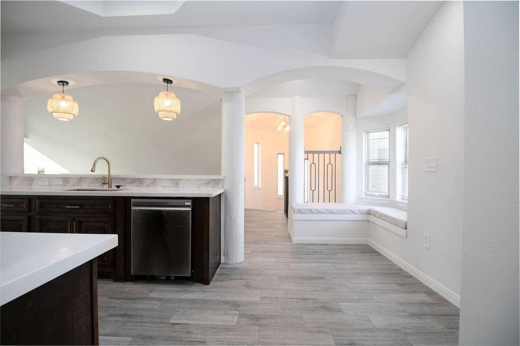 This photo showcases a bright, open kitchen and seating area. It features modern pendant lighting, dark wood cabinetry, and stainless steel appliances. The space includes a cozy window seat and light wood flooring, creating a welcoming atmosphere.