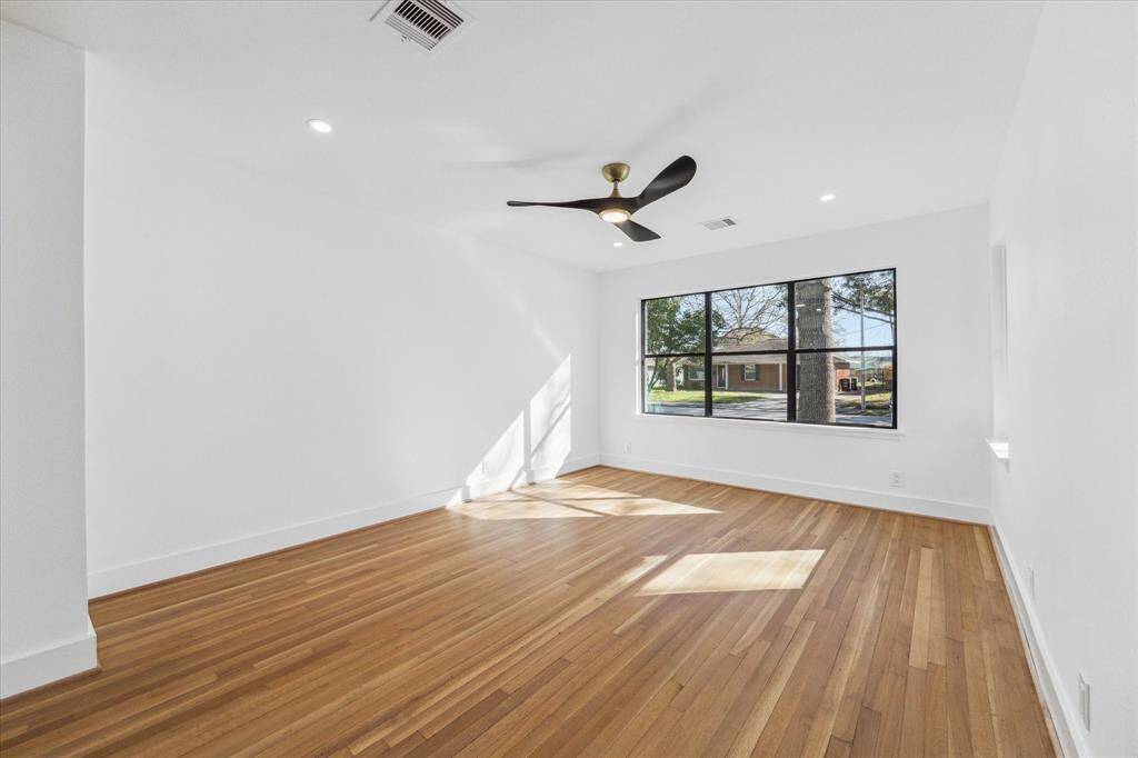 The living area features freshly  painted walls, sleek modern ceiling fan light combo and warm hardwood flooring. This  single large  window provides natural light, offering a cozy and inviting atmosphere.