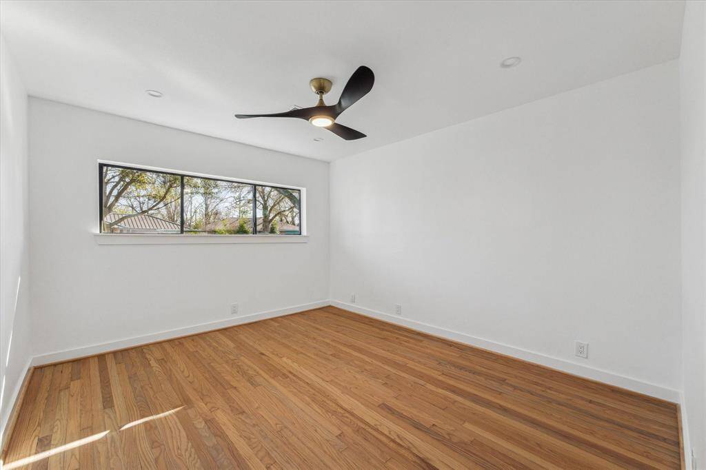 This  primary bedroom offers bright and airy room features hardwood floors, a modern ceiling fan, and a large window with views of trees, offering plenty of natural light.