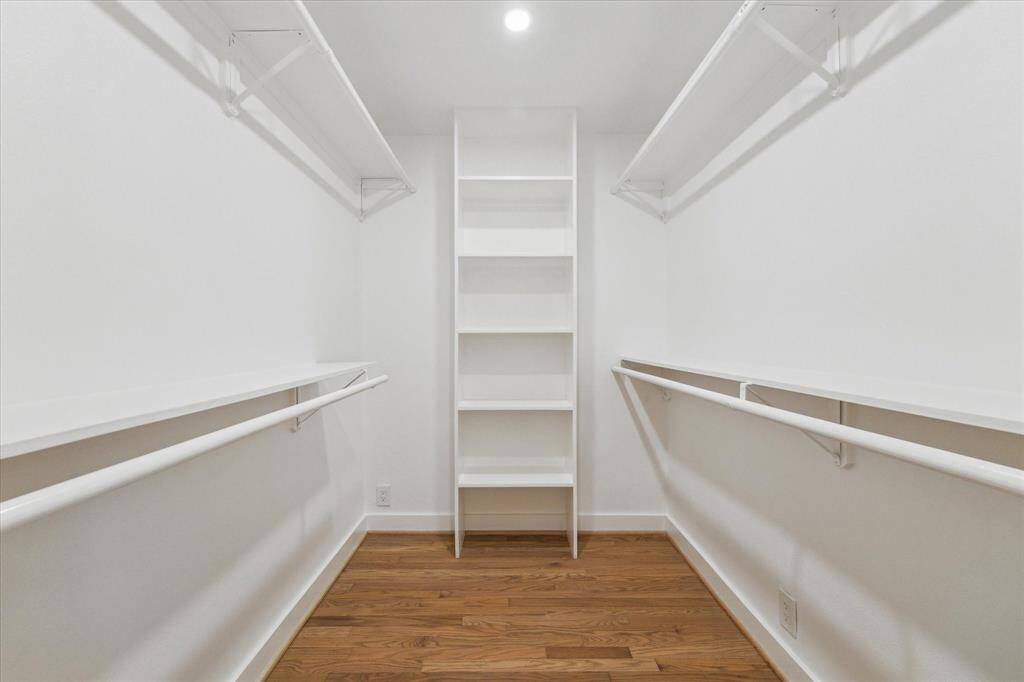 Large and  spacious walk-in closet with wooden flooring, white walls, multiple shelves, and hanging rods for ample storage.