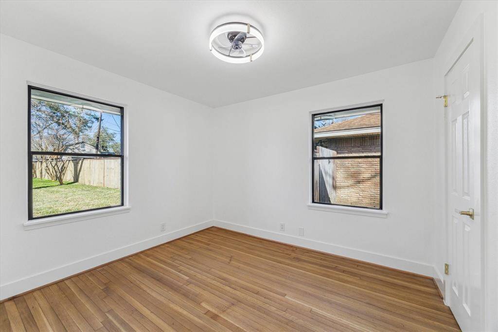 This  large back  bedroom features refinished warm hardwood flooring, illuminated by a modern ceiling light. Two large windows offer plenty of natural light and views of the backyard, creating a bright and inviting space.