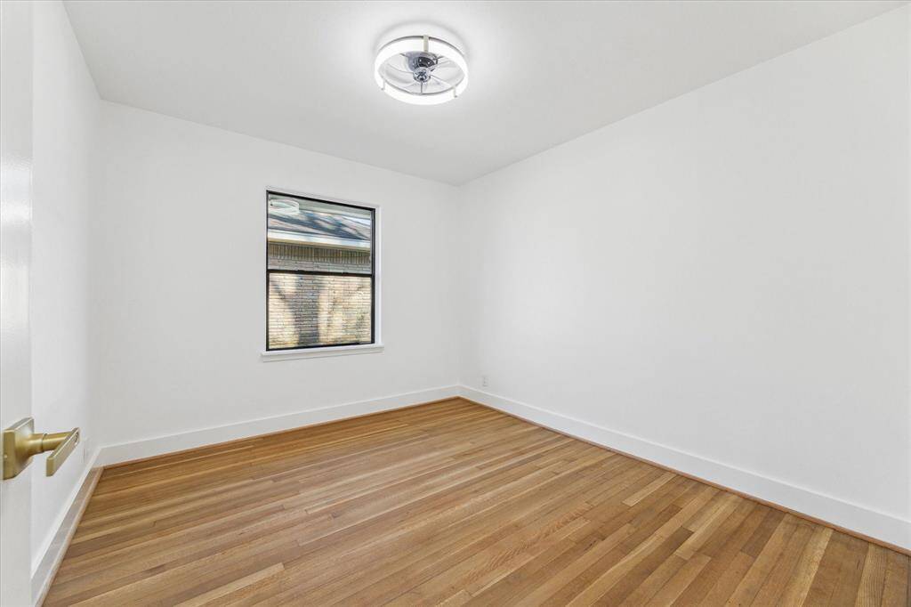 This secondary bedroom features a clean, bright space with white walls and natural wood flooring. The two  windows allow natural light and a modern ceiling light fixture. Perfect for a bedroom or office.