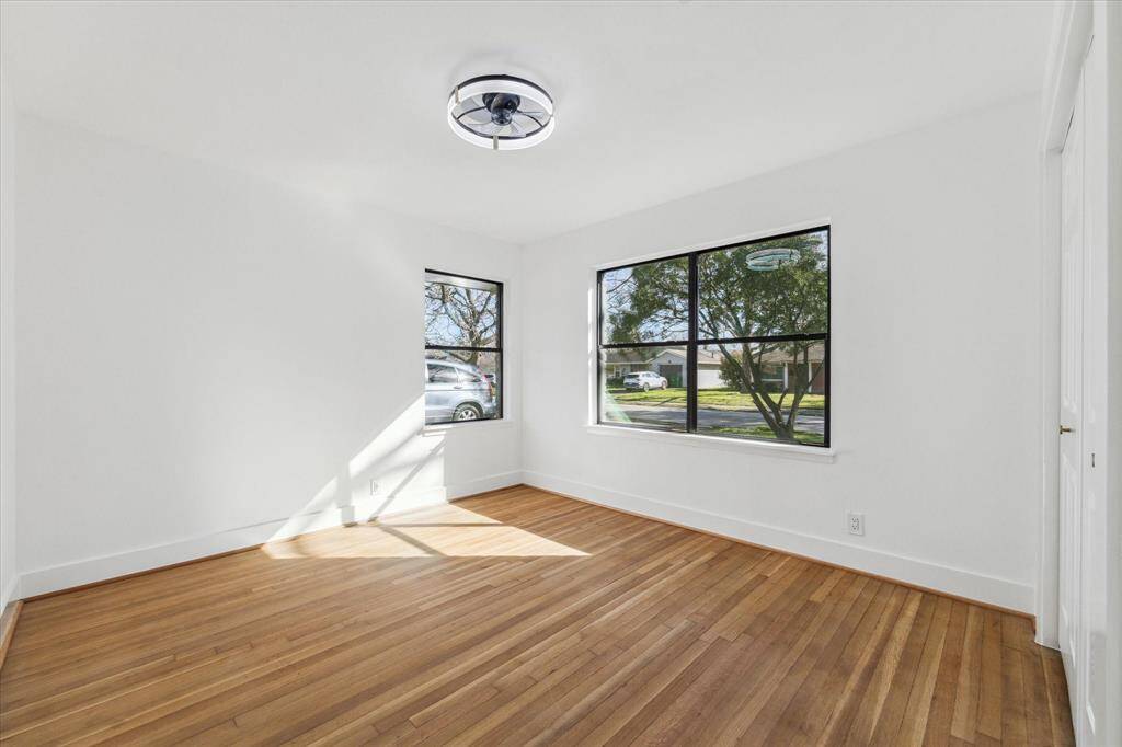 This bright front bedroom features hardwood floors, two large windows with views of the front yard, and a modern ceiling light, creating a fresh and inviting space.