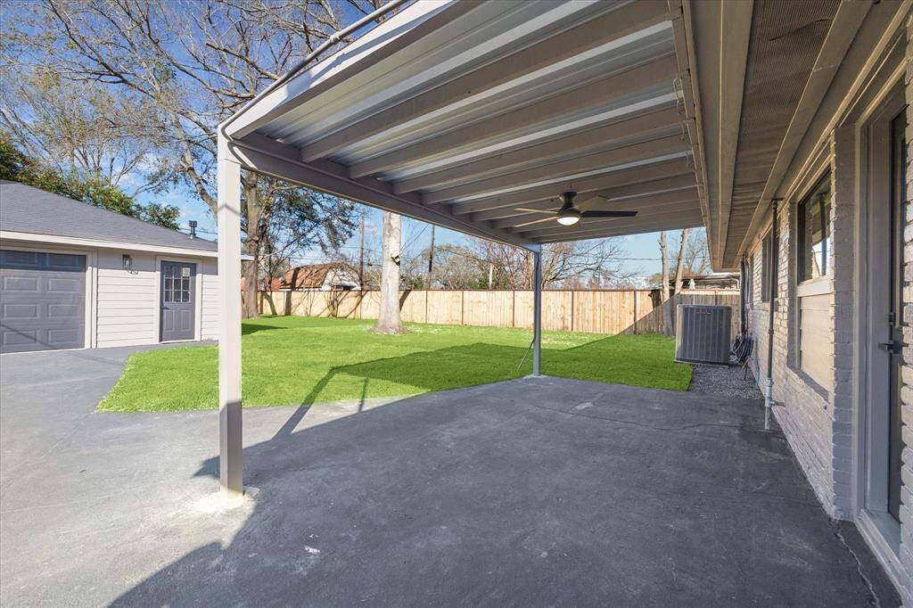 This photo showcases a backyard with a covered patio featuring a ceiling fan, perfect for outdoor relaxation. There is ample space for all your furbabies as well.  The space includes a well-maintained lawn, privacy fence and an over-sized detached garage , offering a versatile and inviting area for outdoor activities.