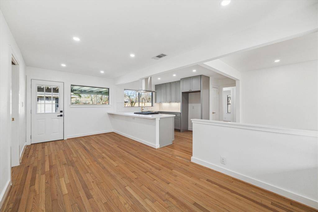 This modern kitchen features sleek gray cabinets, stainless steel appliances, and a large farmhouse sink. The light hardwood floors and ample natural light create a breakfast area.