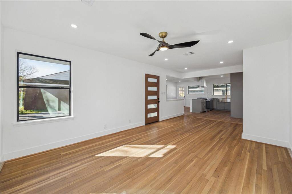 This photo showcases a bright, open and spacious floorplan with  refinished hardwood floors. It features a modern wooden door with frosted glass panels and recessed lighting. The space is ideal for a living area.