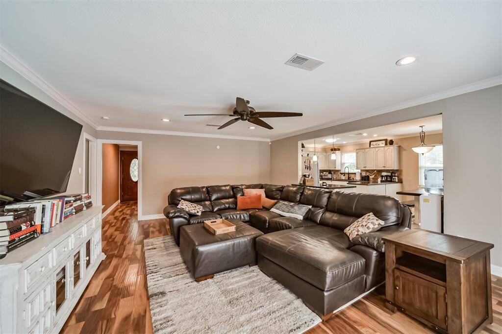 This cozy living room features a large sectional sofa, hardwood floors, and a mounted flat-screen TV. Natural light flows in through glass doors, and a ceiling fan adds comfort. Ideal for relaxation and entertaining.