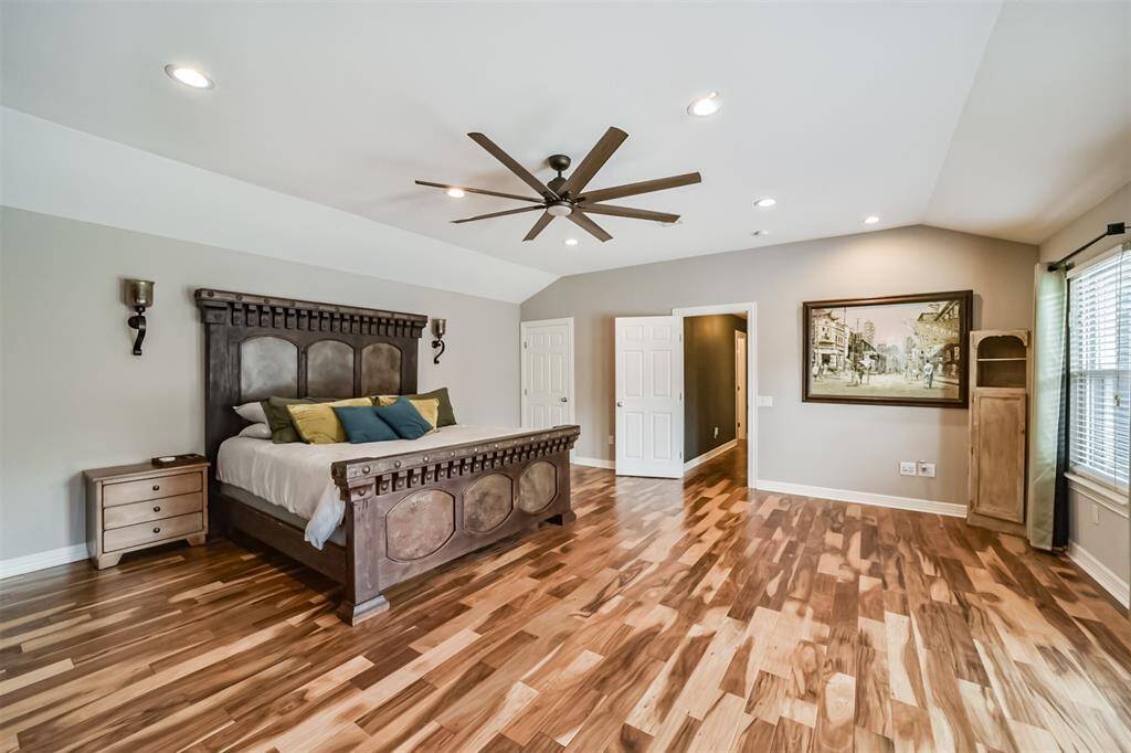 Spacious primary bedroom featuring rich hardwood flooring, a bold accent wall, and a stylish ceiling fan. The room includes an en-suite bathroom and mounted TV, offering comfort and convenience.