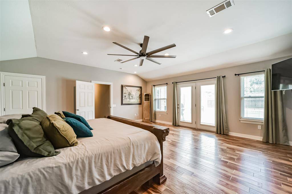 The primary is bright bedroom with hardwood floors, large ceiling fan, and multiple windows for natural light. Features double French doors leading to the outside, creating an inviting and airy atmosphere.