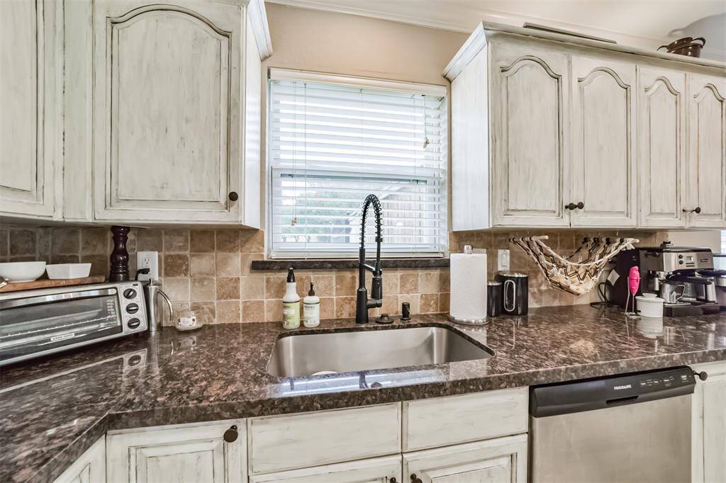 This kitchen features elegant dark granite countertops, light cabinetry, and stainless steel appliances. It has ample counter space, ambient lighting, and a tiled floor, creating a cozy and functional cooking area.