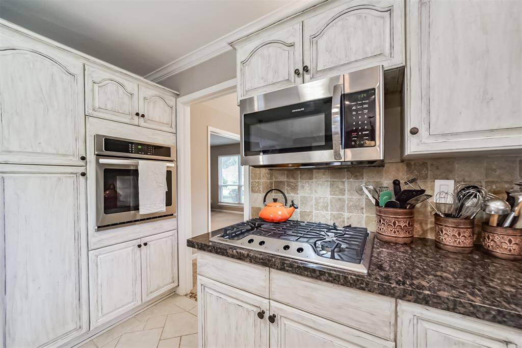 This kitchen features elegant cabinetry, a built-in oven, and a microwave. It has a gas cooktop with a stylish backsplash and ample counter space for cooking.