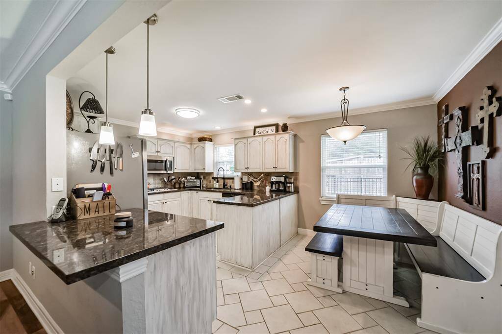 This inviting living room features a spacious layout with a large sectional sofa, wood flooring, and a ceiling fan. It opens to the kitchen, creating a seamless flow. A wall-mounted TV and cozy decor complete the space.
