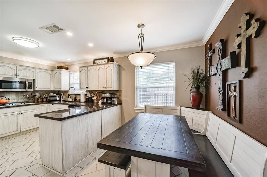 This kitchen features rustic cabinetry with a matching island and dark countertops. It includes a cozy breakfast nook with a wooden bench and table, accented by a decorative wall. The space is bright and welcoming, ideal for family gatherings.