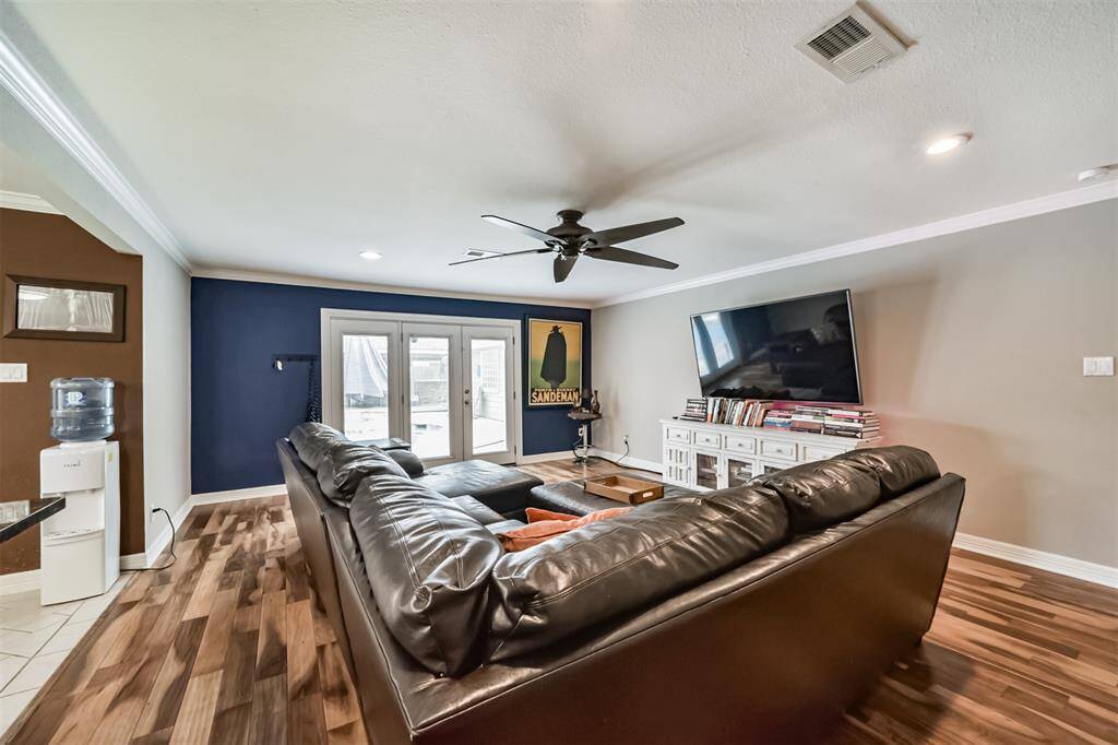 This spacious living room features hardwood floors, and a ceiling fan. French doors lead to a patio, and the room is open to a kitchen area with pendant lighting. A modern decor and ample natural lightThis inviting living room features a spacious layout and opens to the kitchen, creating a seamless flow. A wall-mounted TV and cozy decor complete the space.  TV could be included.