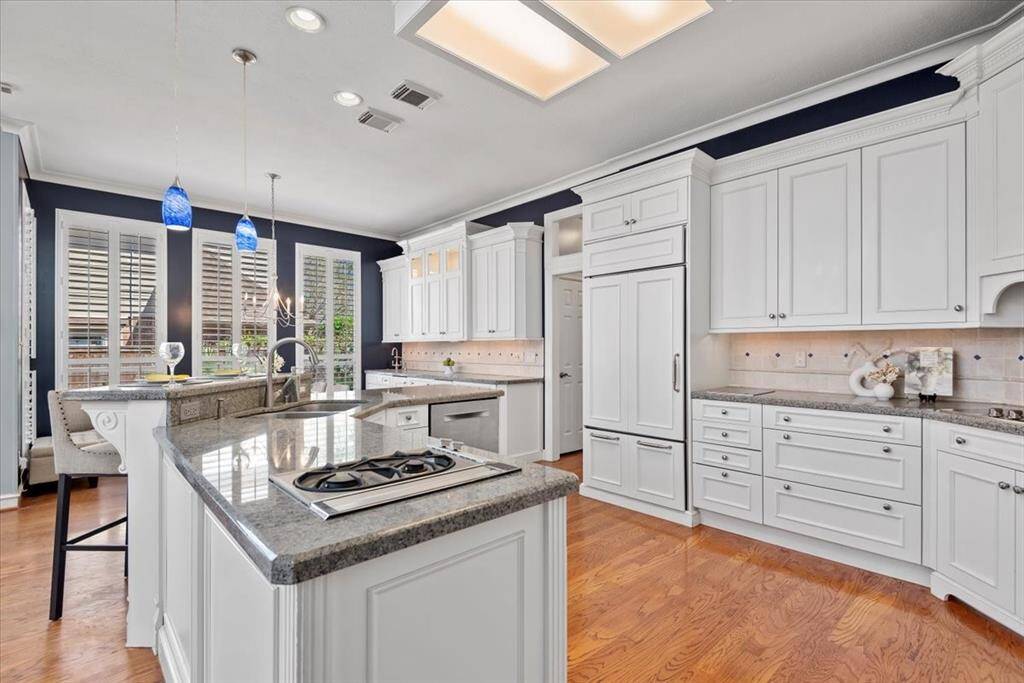 This spacious and modern kitchen features white cabinetry, granite countertops, upgraded appliances, and a central island with seating.