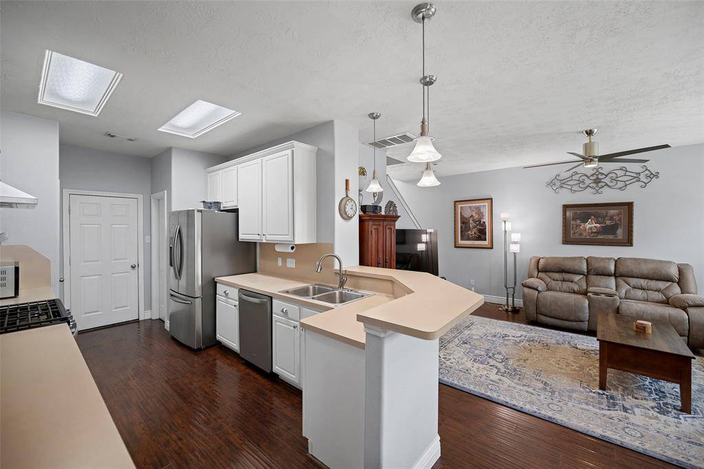 Open-concept living space featuring kitchen with stainless steel appliances, white cabinetry, and dark hardwood floors. The kitchen island overlooks the cozy living area.